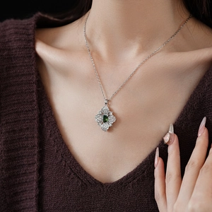 Close-up of a silver flower necklace featuring an emerald green center stone on a model