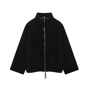Detail of black faux shearling texture, metal zipper, and large patch pockets on a high collar jacket