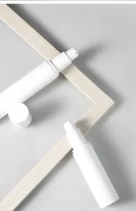 Detail view of two white cylindrical cosmetic pump bottles on a minimalist wooden frame