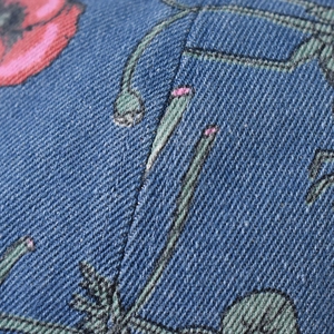 Macro detail of blue denim fabric with vibrant red poppy flower embroidery on baseball cap