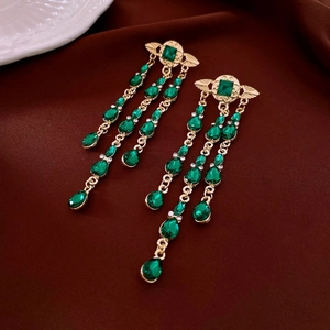 Macro view of gold tassel earrings with green gemstones and wing design on silk