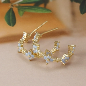 Macro detail of gold flower hoop earrings with light blue stones and C-shaped design
