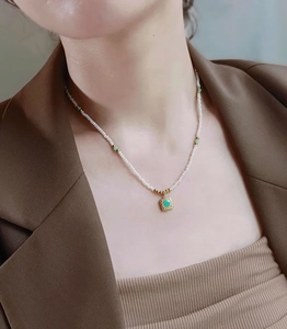 Detalle del collar de perlas con colgante cuadrado dorado e incrustación de piedra verde