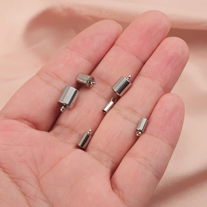 Silver cylindrical metal end caps for DIY jewelry held in hand on pink silk background