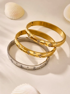 Macro detail of polished stainless steel bangles with clover-shaped zircon inlays