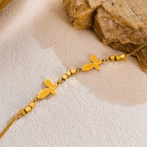 Détail du bracelet papillon doré avec perles carrées sur fond de pierre naturelle