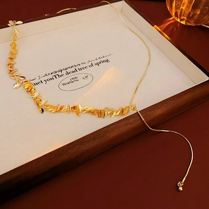 Detailed view of a gold leaf tassel necklace on a white wooden display tray