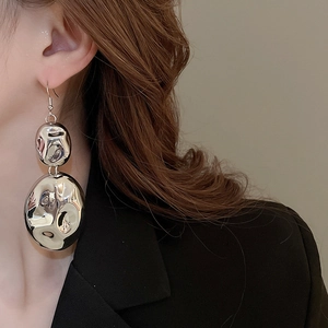 Close-up of oversized silver textured drop earrings with liquid metal aesthetic on model
