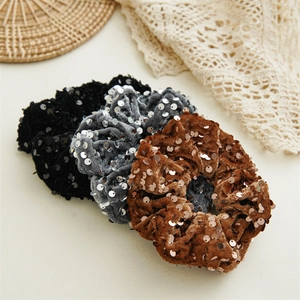 Close-up of three sequined velvet scrunchies in black, silver, and caramel brown colors