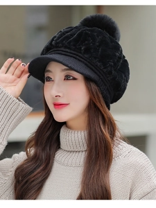 Detail of a black knit beanie featuring a large plush faux fur pompom and a knitted brim