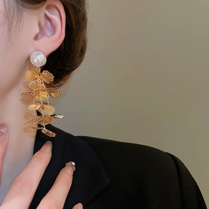 Detail view of hollow gold floral tassel earrings with white pearls worn by a model