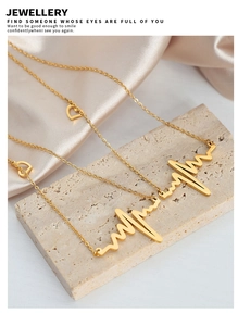Detailed view of gold heartbeat pendant necklace with heart elements on stone surface