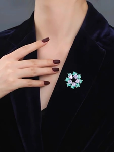 Close-up of a floral brooch with purple and green stones on a blue velvet blazer lapel