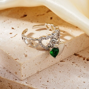 Exquisite silver heart ring with green gemstone pendant on beige stone display
