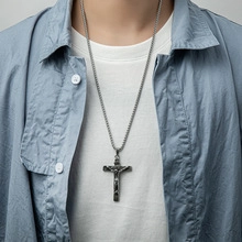 Close-up of a silver crucifix pendant on a round link chain worn by a male model