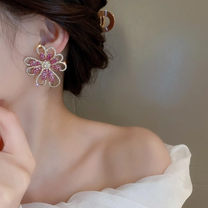 Detail eines übergroßen goldene Blumenohrrings mit rosa Kristallen an einem Modell