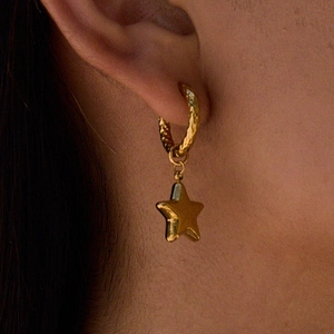 Close-up of golden textured hoop earring with star pendant worn on earlobe