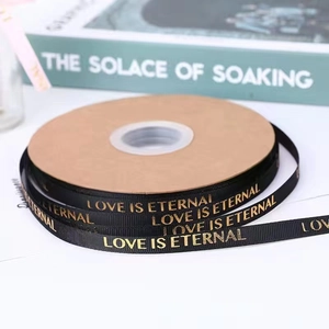 Macro view of black ribbon with gold Love is Eternal foil printing for gift wrapping