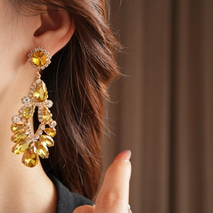 Close-up of model wearing luxury gold-toned teardrop tassel earrings with yellow crystals