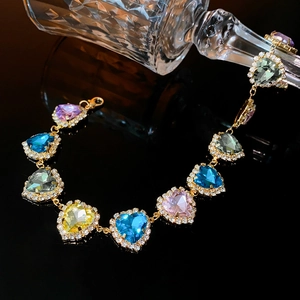 Close-up of gold chain bracelet with colorful heart-shaped gems on dark reflective surface