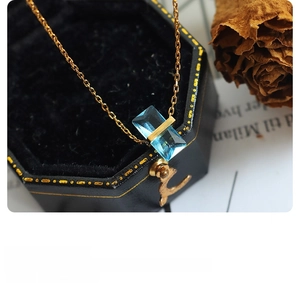 Macro shot of a gold chain necklace with a blue rectangular crystal pendant on a black box