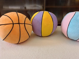 Detailed close-up of soft plush basketball pillows in orange, yellow, and blue colors