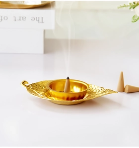 Detailed macro view of golden leaf-shaped incense burner with burning cones on a clean desk