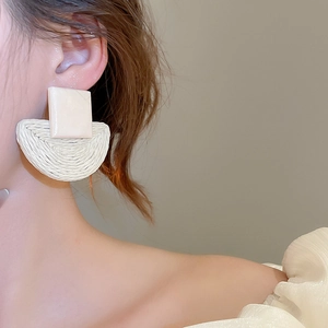 Detail of raffia woven semicircular earrings with a square resin top on woman's profile