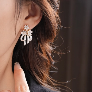 Gros plan de boucles d'oreilles fleur dorées avec nœud blanc et zircons brillants