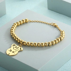 Close-up of golden beaded bracelet with pig pendant and lobster clasp on jewelry display