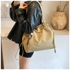 Detail of khaki drawstring bucket bag with silver clover logo and fringe accents