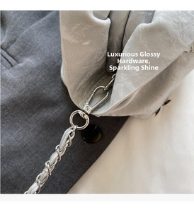 Close-up of polished silver metal clasp and chain on a pleated metallic handbag