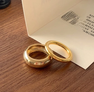 Close-up of minimalist gold polished stacking rings on wooden surface with branding
