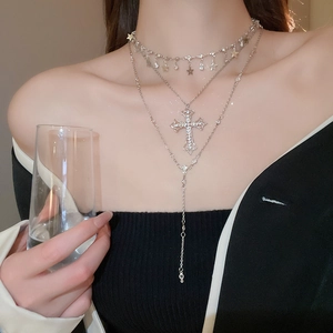 Detail view of layered silver necklace featuring a rhinestone cross and star pendant