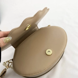Detail of beige PU leather shell bag showing magnetic closure and pearl chain strap