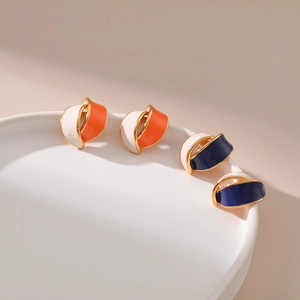 Detailed view of irregular enamel hoop earrings in orange and navy blue on ceramic