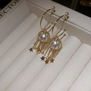 Detail of gold tassel earrings with hollow cage pearls, stars, and zircon accents