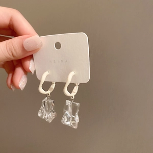 Close-up of irregular clear acrylic ice-cube drop earrings on a white display card