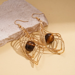 Golden geometric cage earrings with tiger eye stone on textured beige stone background