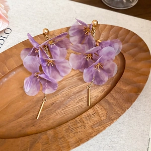 Detailed view of purple fabric flower tassel earrings displayed on a rustic wooden tray