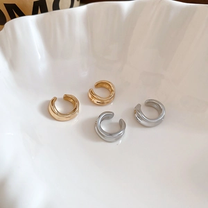 Close-up of polished gold and silver C-shaped ear cuffs on a white ceramic tray