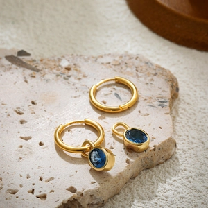 Detail view of gold earrings with detachable blue oval gemstones on textured stone