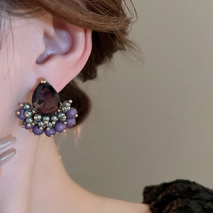 Detail of elegant water drop purple zircon earring on model with golden metal accents