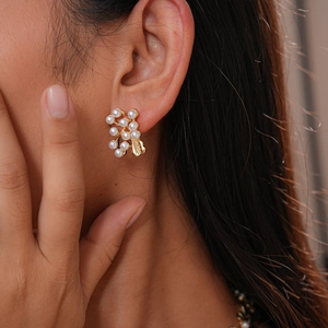 Close-up of golden branch stud earrings with white pearls on a model's ear
