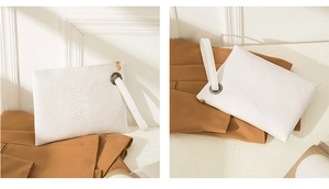 Close-up of white crocodile pattern briefcase with metal ring and handle on a beige blazer