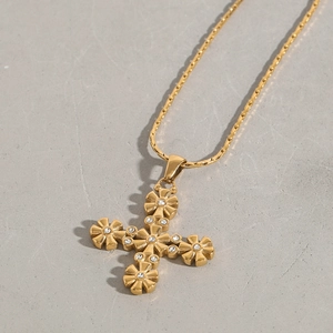 Dettaglio di una collana con pendente a croce dorata con motivi floreali e zirconi