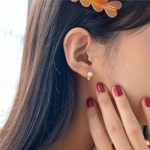 Close-up of elegant pearl drop earring with gold sphere base on female model