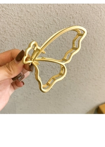 Detail view of a matte gold butterfly-shaped metal hair claw with hollow wing patterns