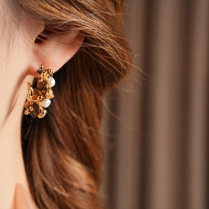 Macro detail of C-shaped flower earrings with tiger eye stones and white pearls on gold metal
