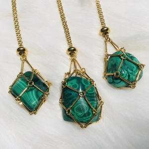 Close-up of golden cage pendants with green malachite stones on a white plush surface
